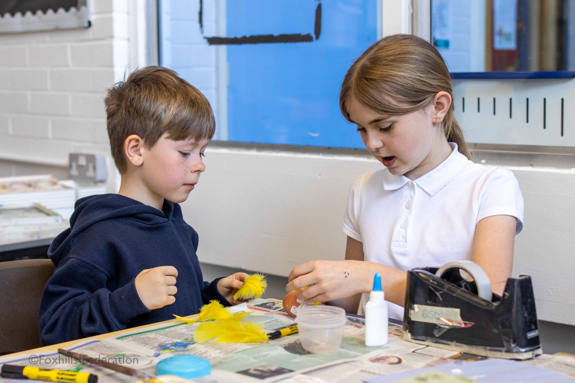 A Year 6 girl helps a boy attach feathers to an egg