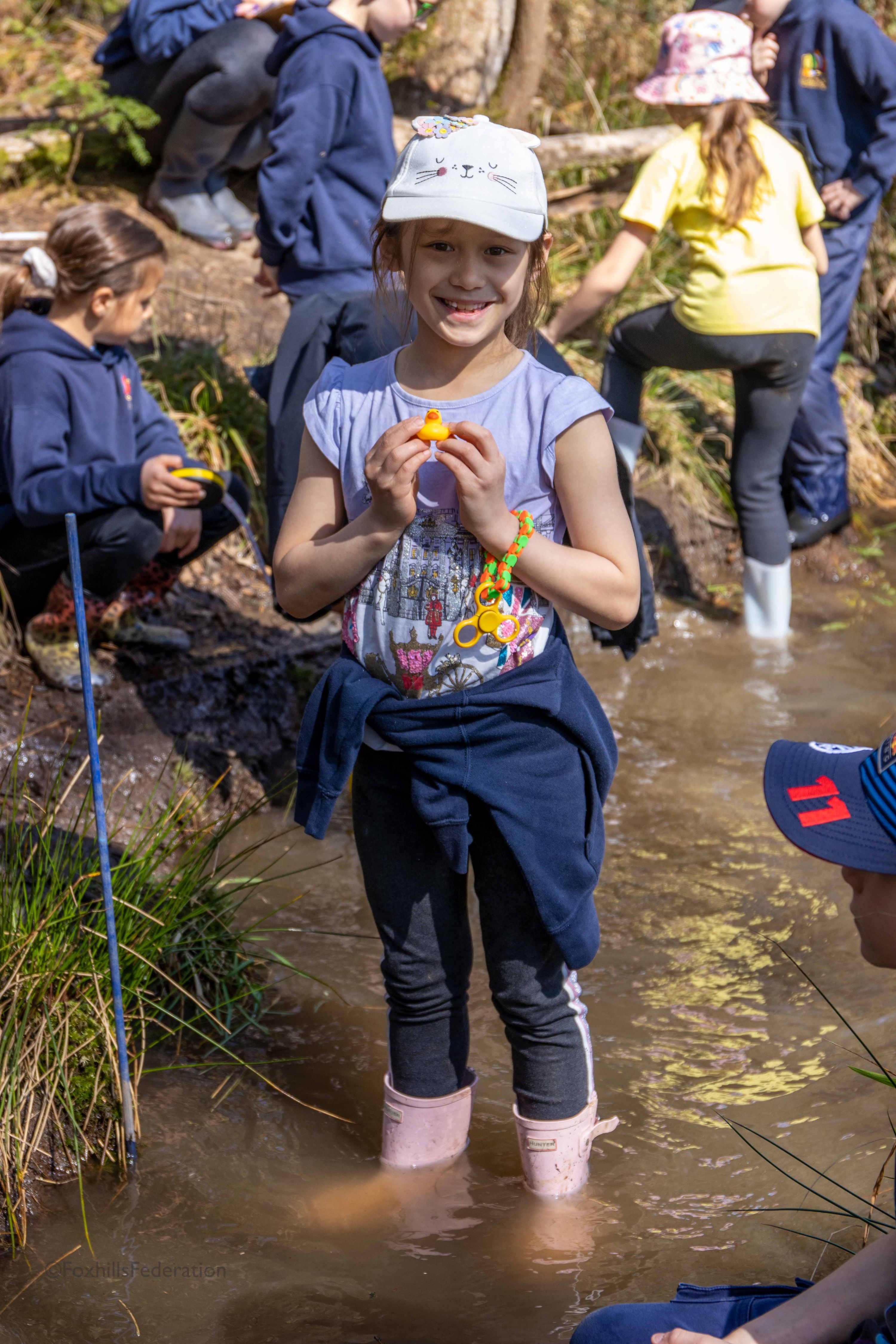 A girl holds a rubber duck while stood in the river