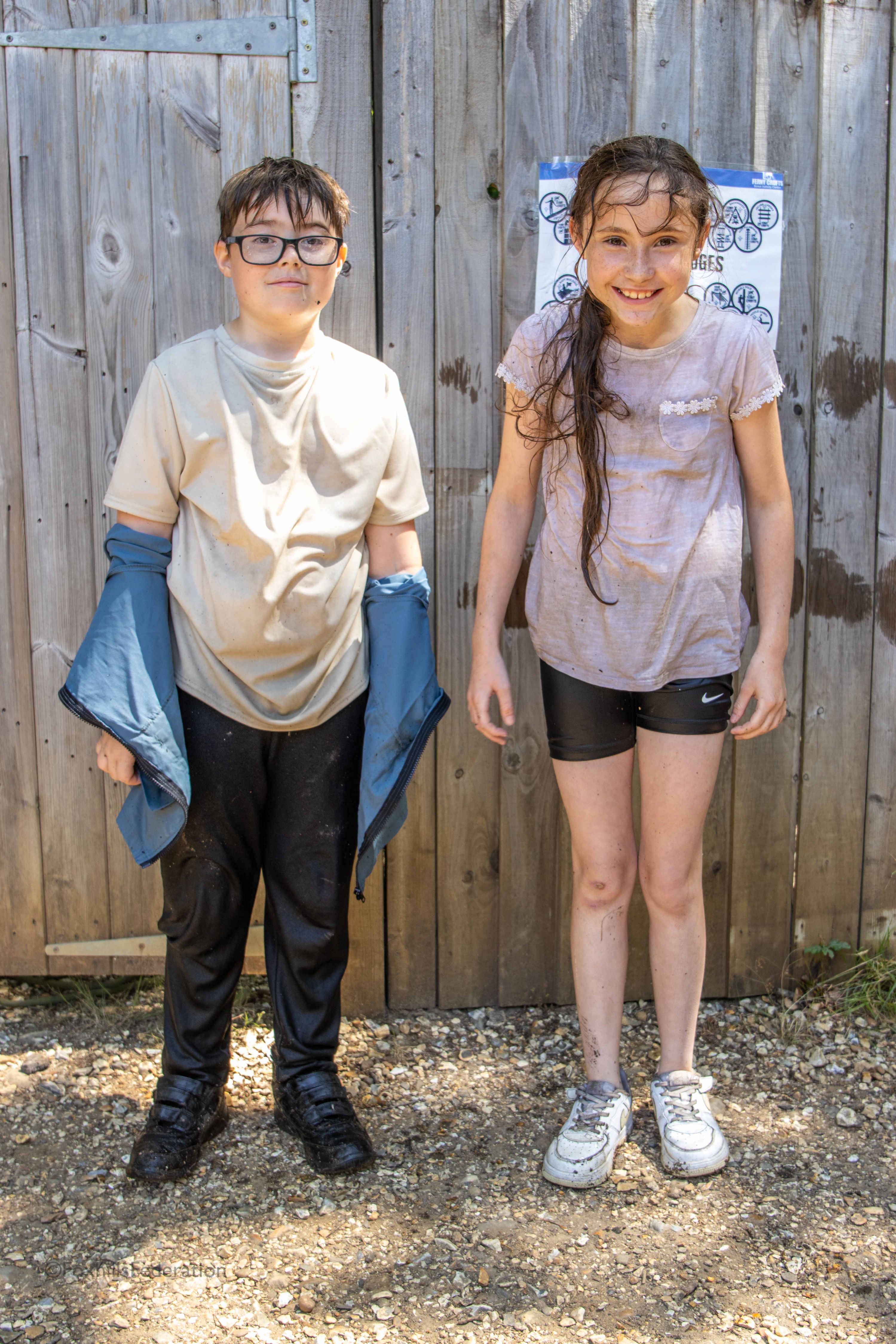 Two children stand soaking wet after raft building