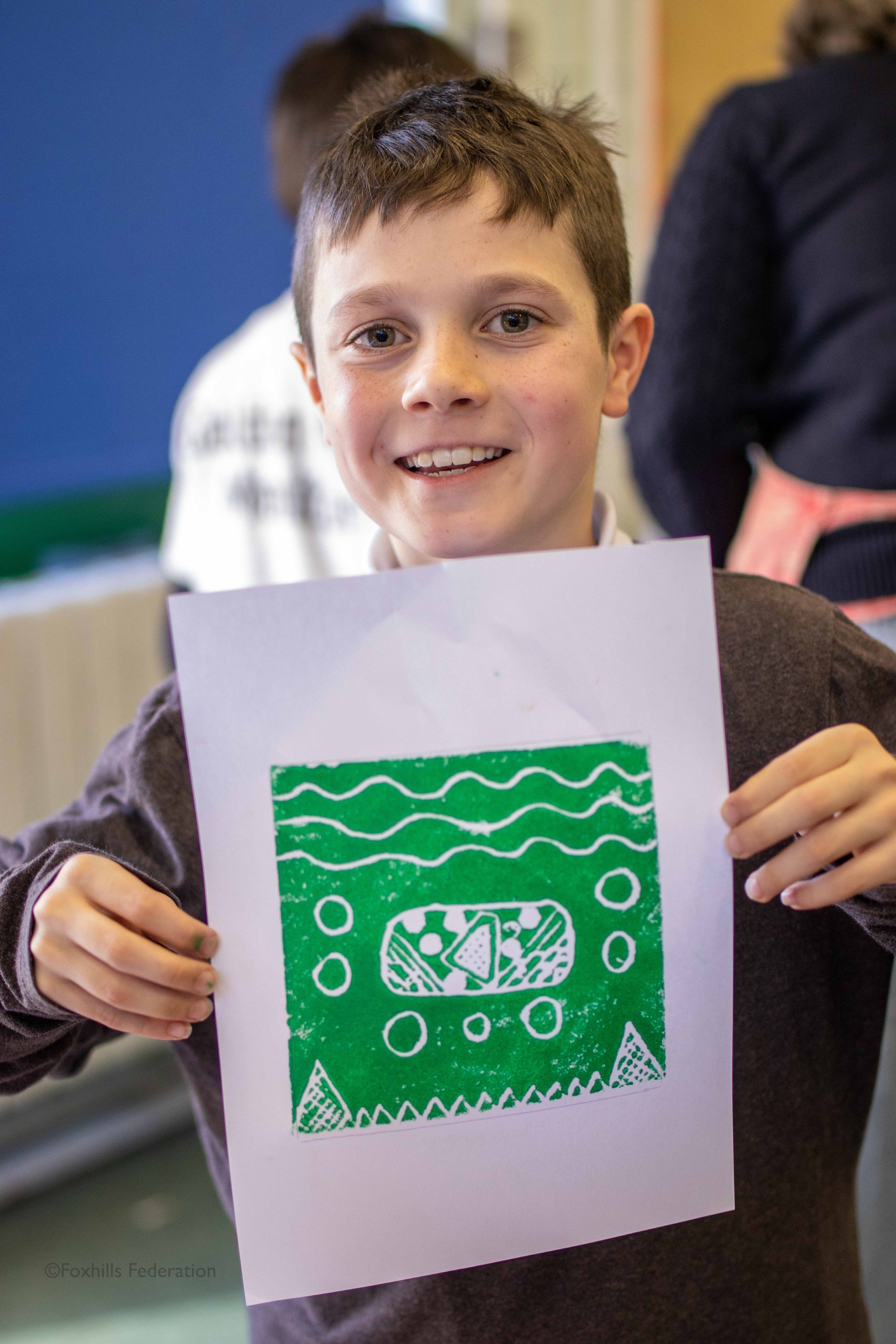 A boy holds up work created by stamp printing.