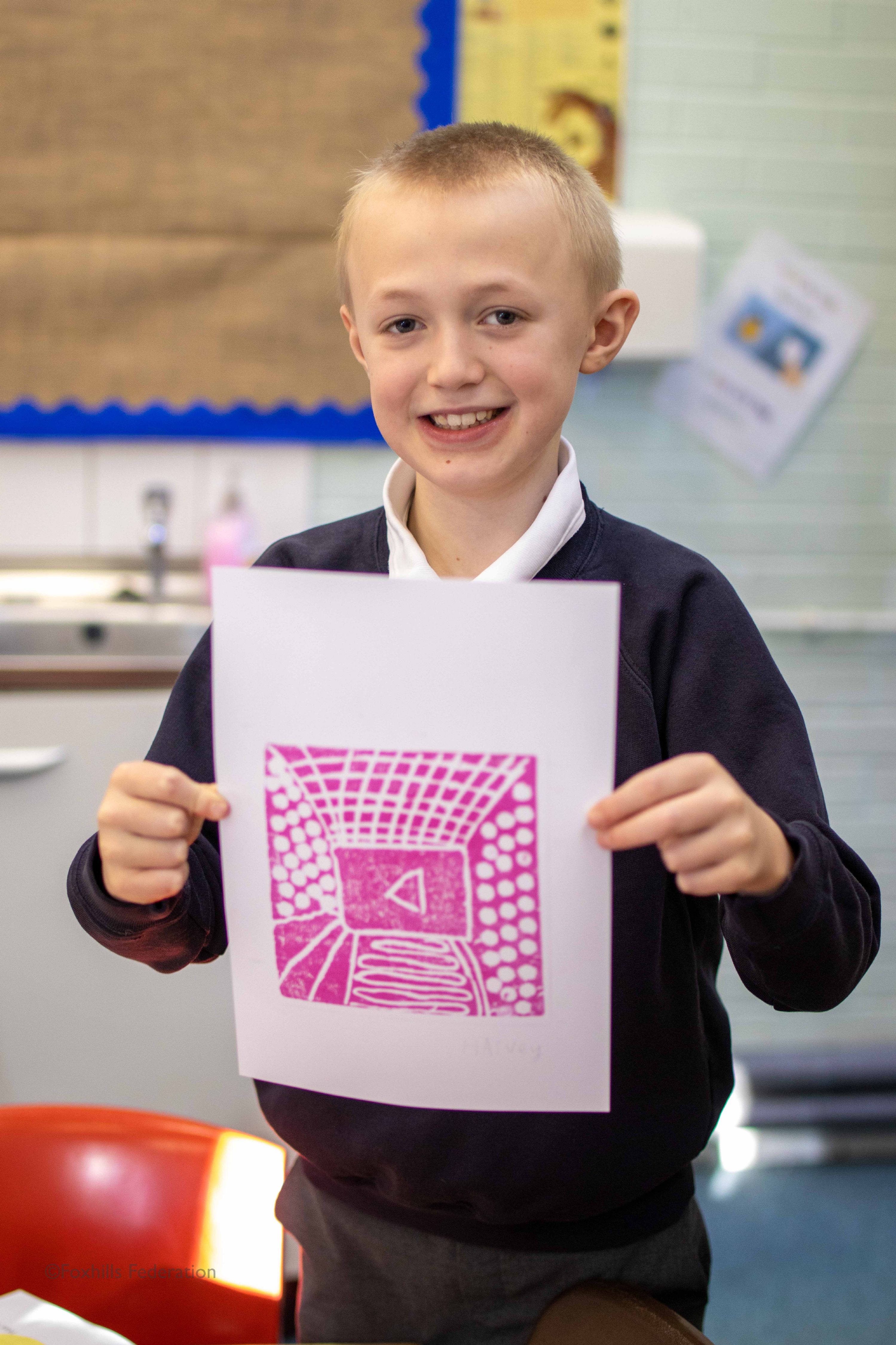 A boy holds up work created by stamp printing.