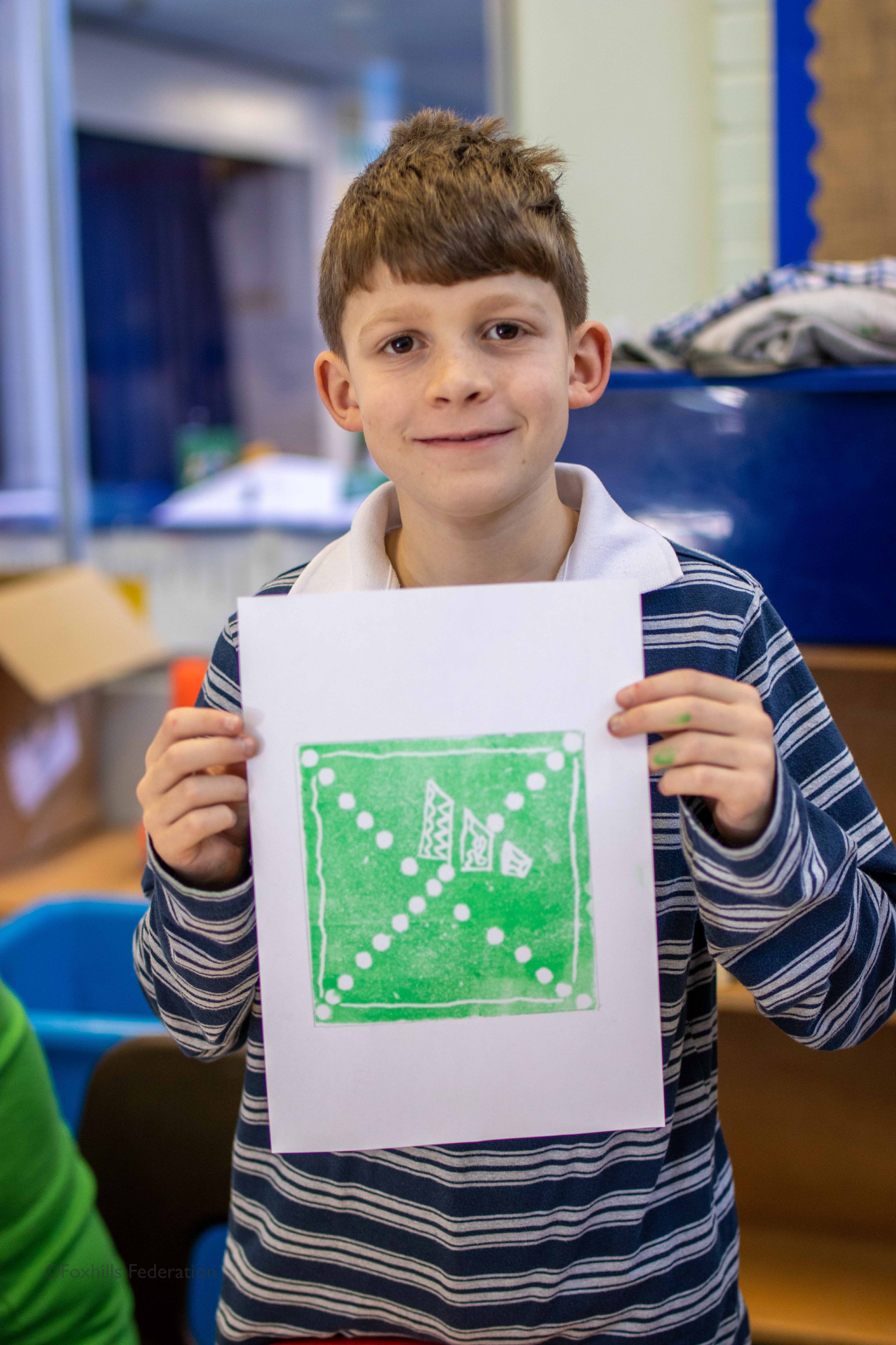 A boy holds up work created by stamp printing.