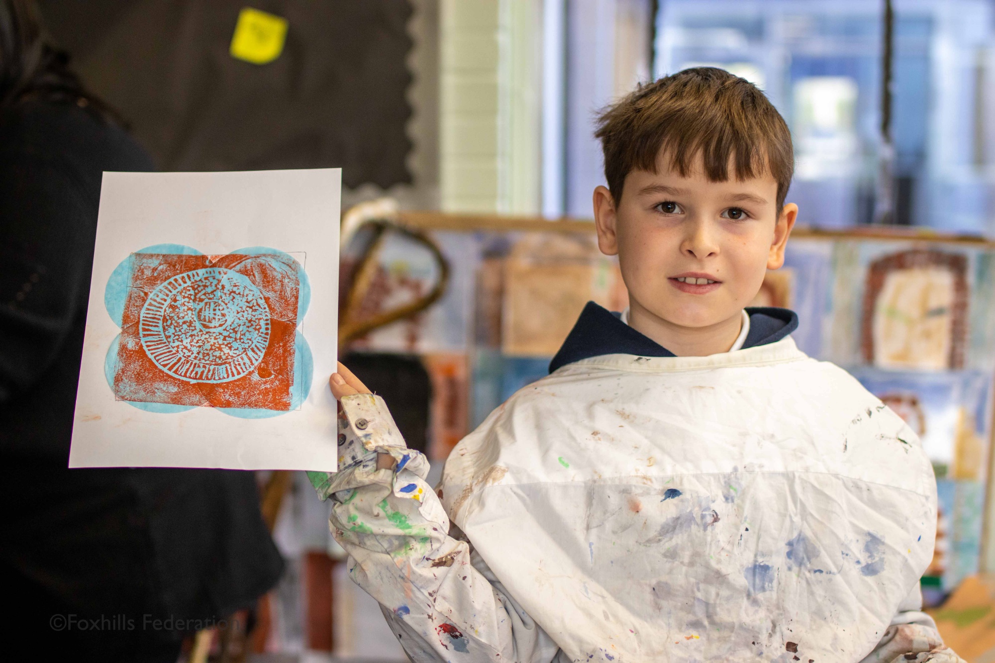 A boy holds up work created by stamp printing.