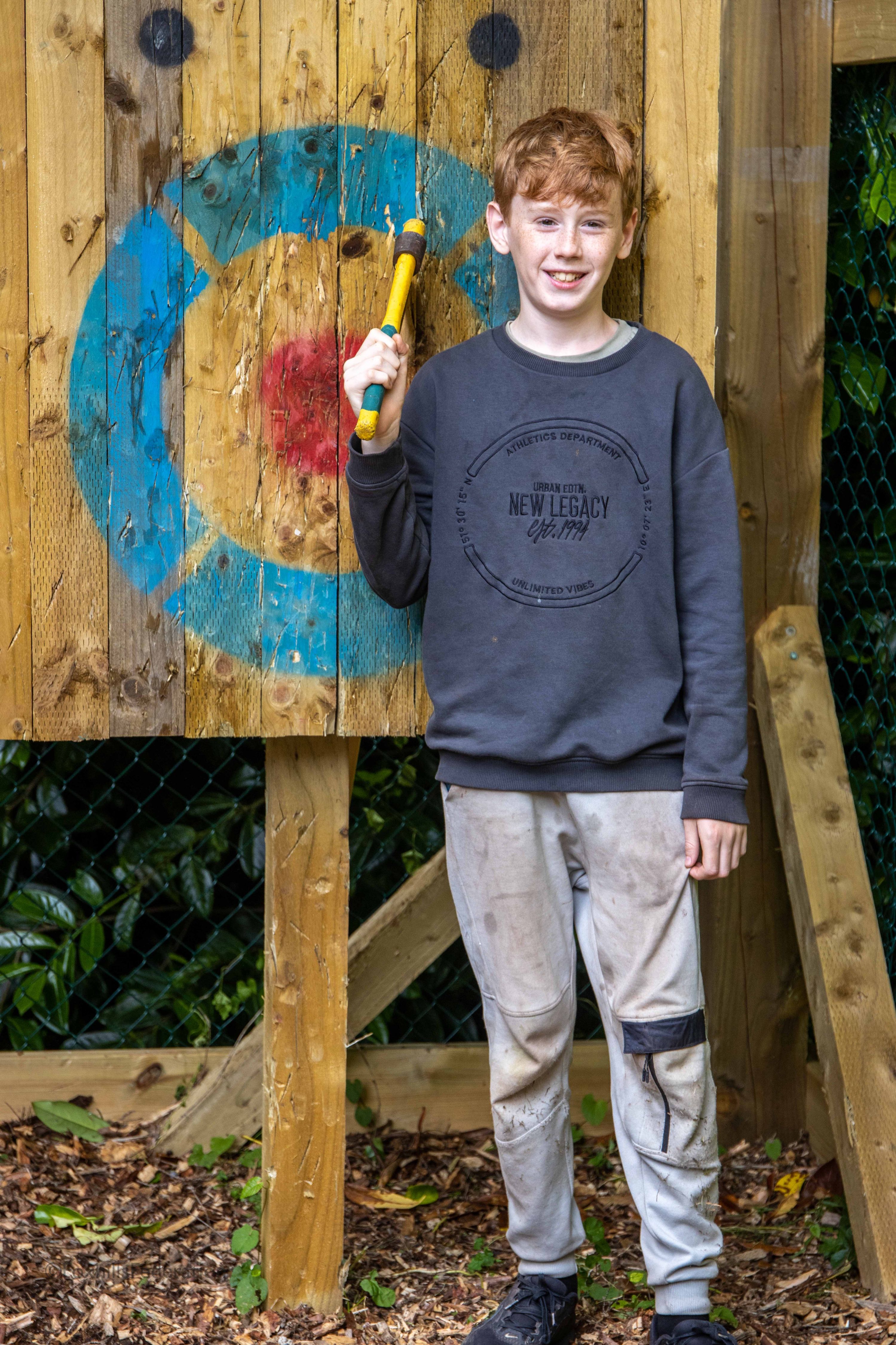 A boy poses with a axe he has just thrown