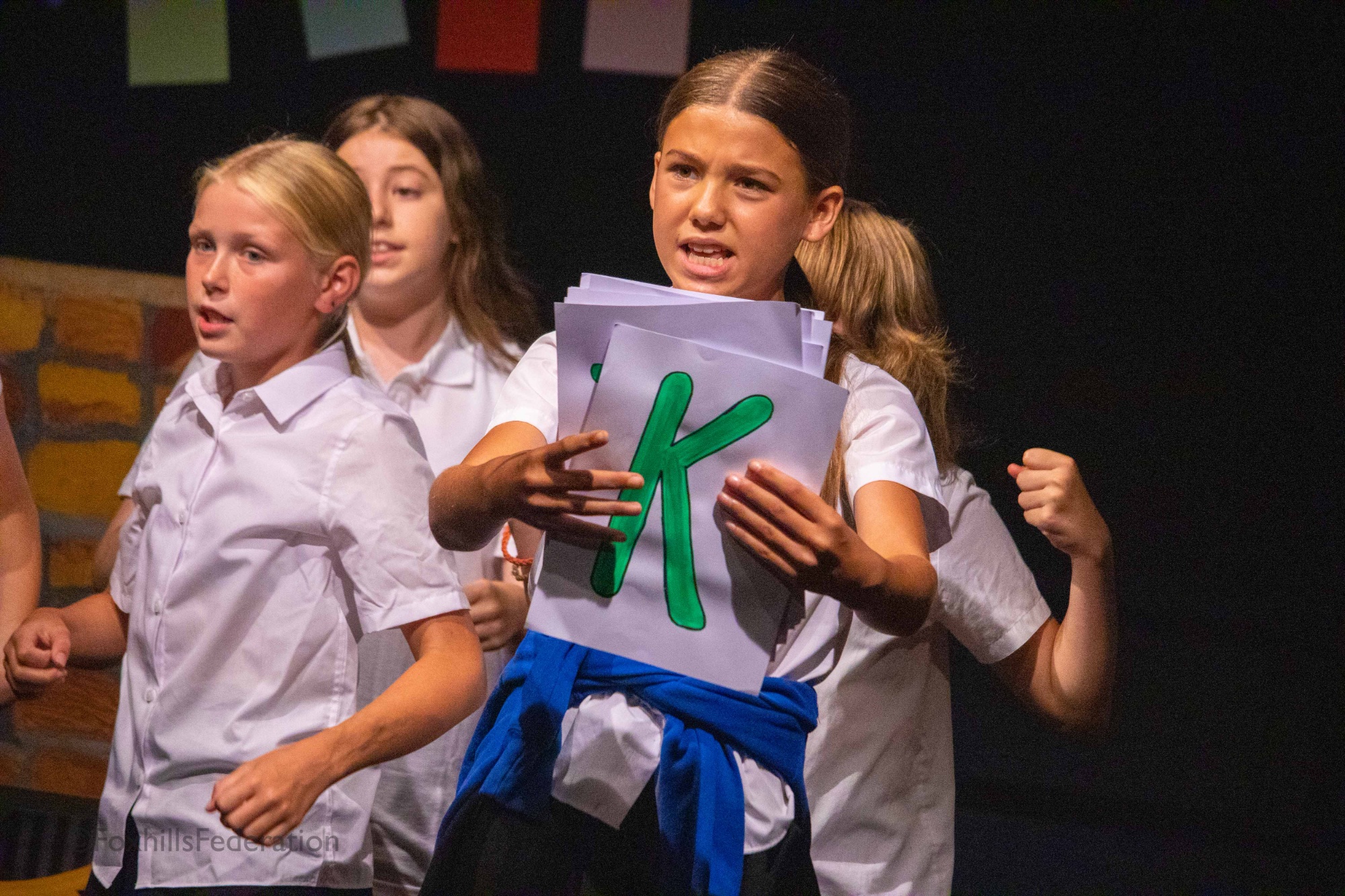 A girls hold up the letter "k" as part of a dance