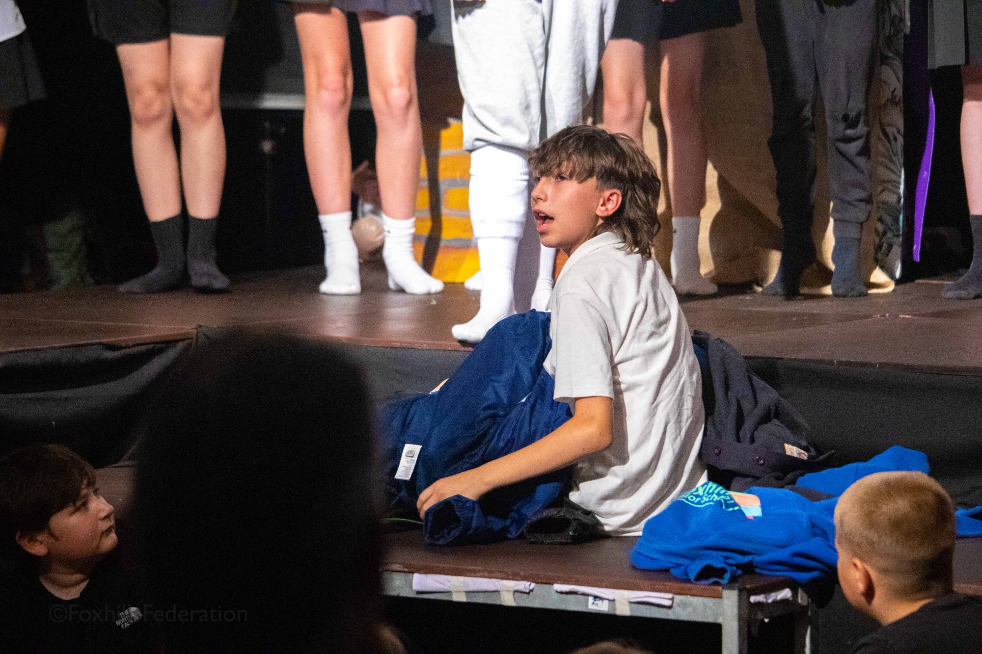 A child hides under a pile of school jumpers