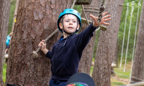 A boy grabs at a rope on a low rope course